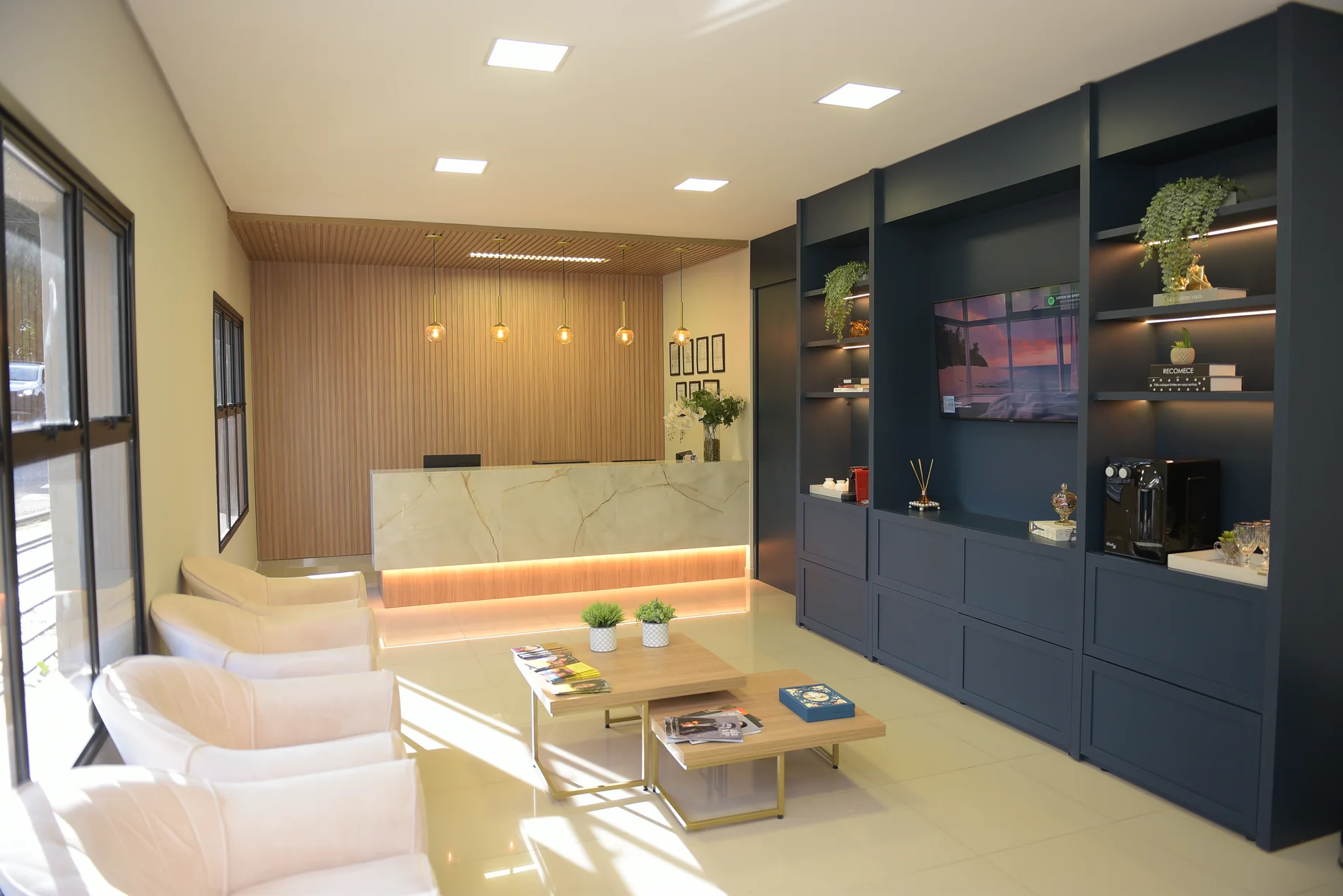 Recepção da Pinhatari Odontologia, com poltronas claras, balcão de mármore e marcenaria azul